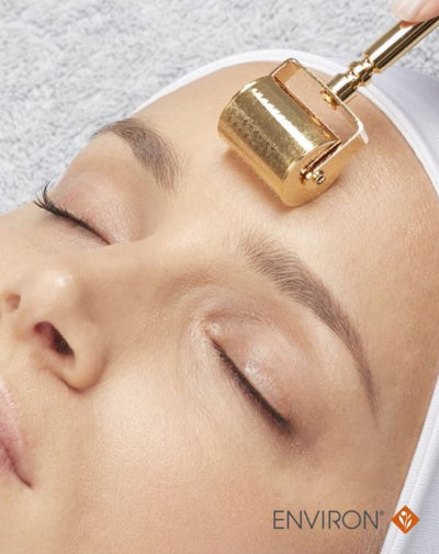 Gold-toned roller device with a cylindrical head and handle, designed for facial treatment