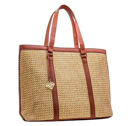 A stylish woven straw tote bag features brown faux-leather trim, long shoulder straps, and a gold logo charm against a white background.