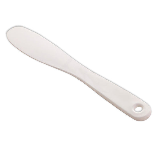 A white plastic sandwich spreader with a rounded blade and a hanging hole rests on a light surface.