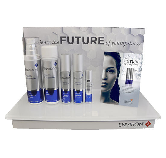 A collection of Environ Youth EssentiA anti-aging skincare products, including serum and toner, sits on a branded retail display stand promoting the future of youthfulness.